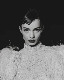 Portrait of a woman with dark hair and fringe wearing a feathered high-neck garment against a black background.