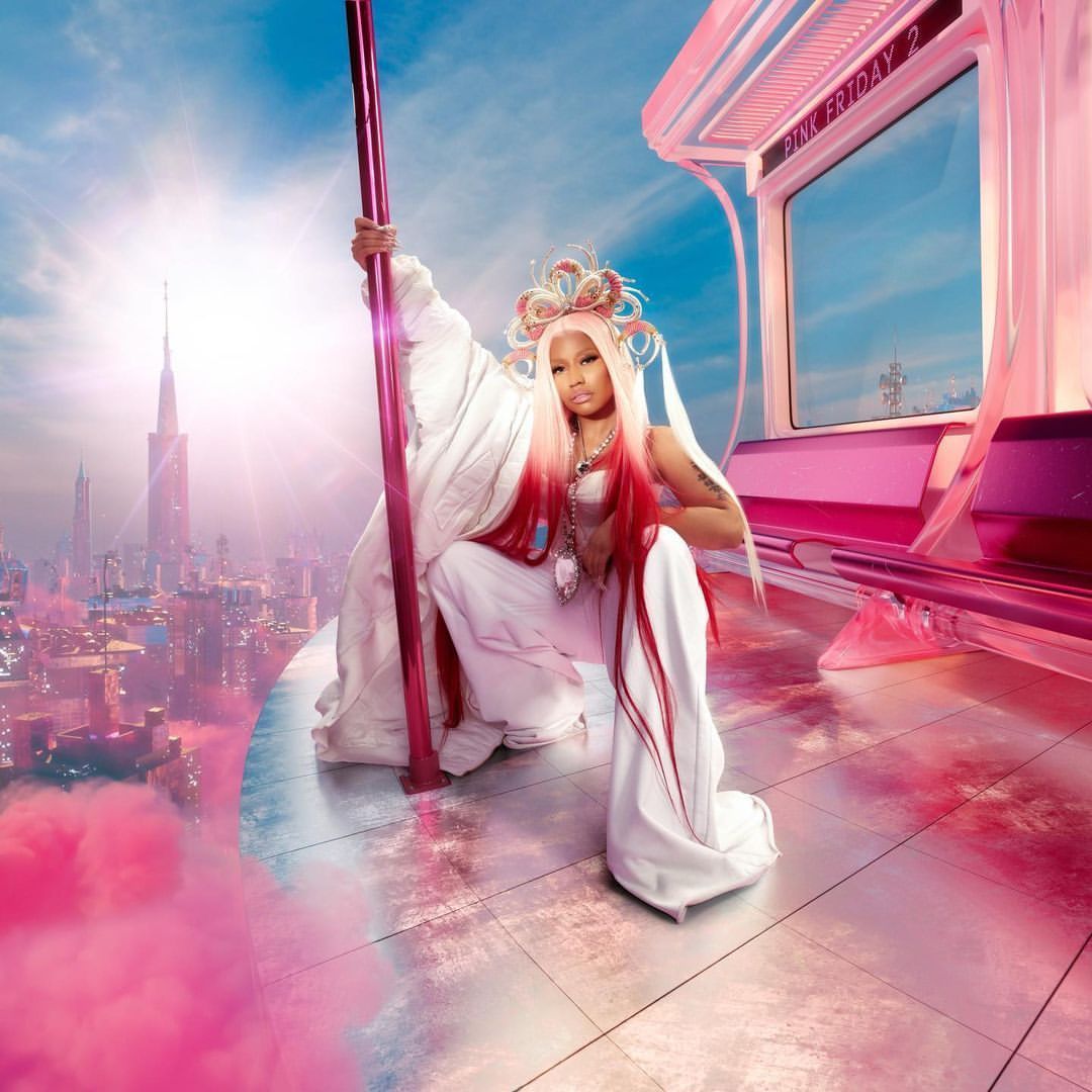 Nicki Minaj posing in white outfit against futuristic city backdrop with pink accents, next to pink subway car and pink pole.