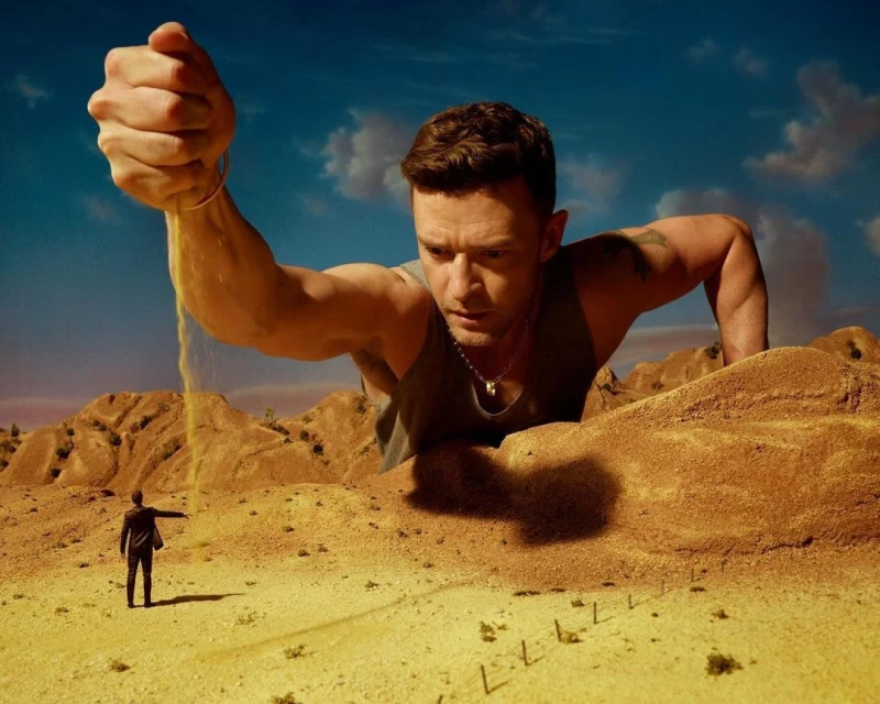 Artistic image of a large man pouring sand over a desert landscape with a small person in the background, set against a blue sky.