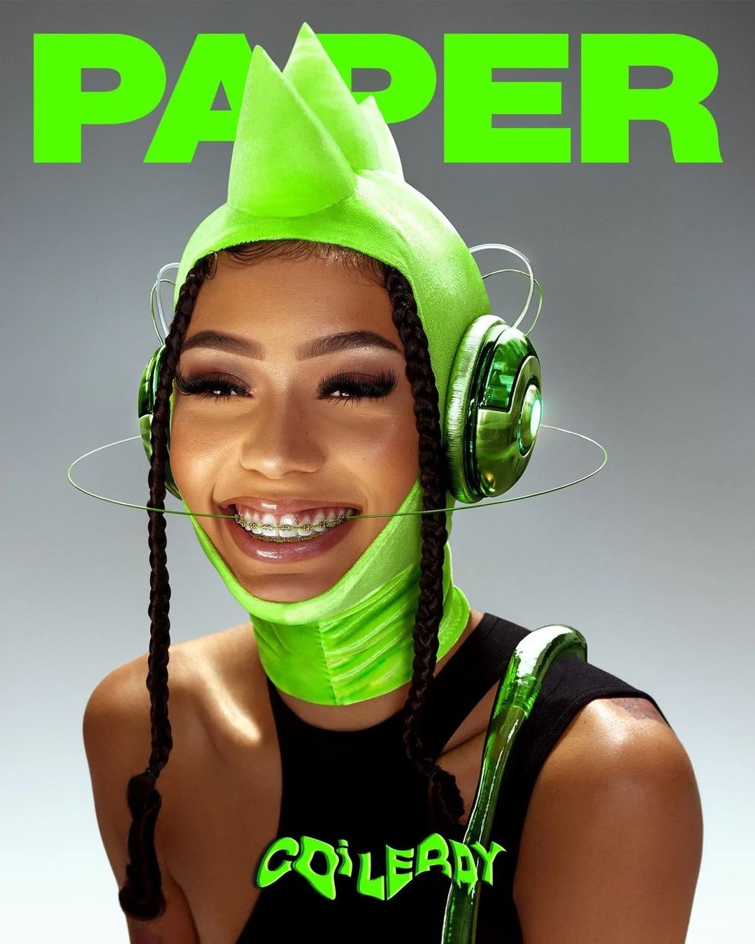 Close-up shot of a smiling woman with braids wearing braces, a neon green hat-mask, and a black top, featuring the word 'PAPER' on top.
