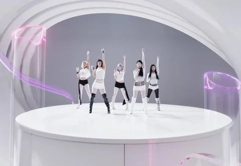 Five women in coordinated white outfits pose on a white platform under studio lighting with purple translucent design elements, smiling.