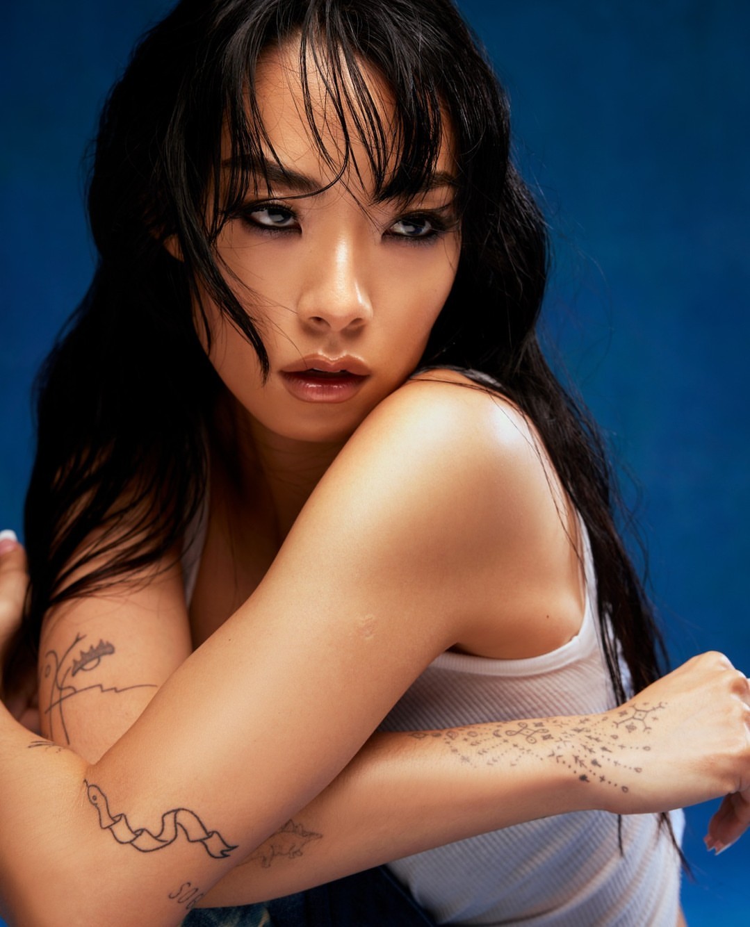 Close-up portrait of a woman with dark hair wearing a white tank top against a deep blue textured background