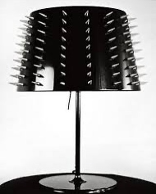 Black table lamp with spike accents, standing on a circular base against a bright white background, creating a high-contrast minimalist design.