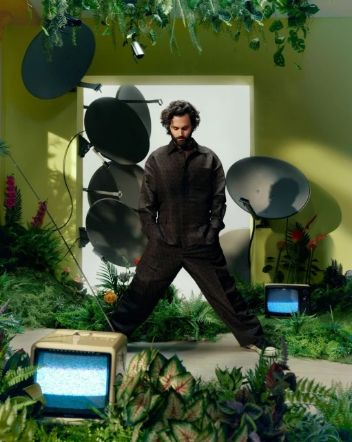 Indoor portrait of a man in patterned suit surrounded by satellite dishes, ferns and vintage television sets in a studio.