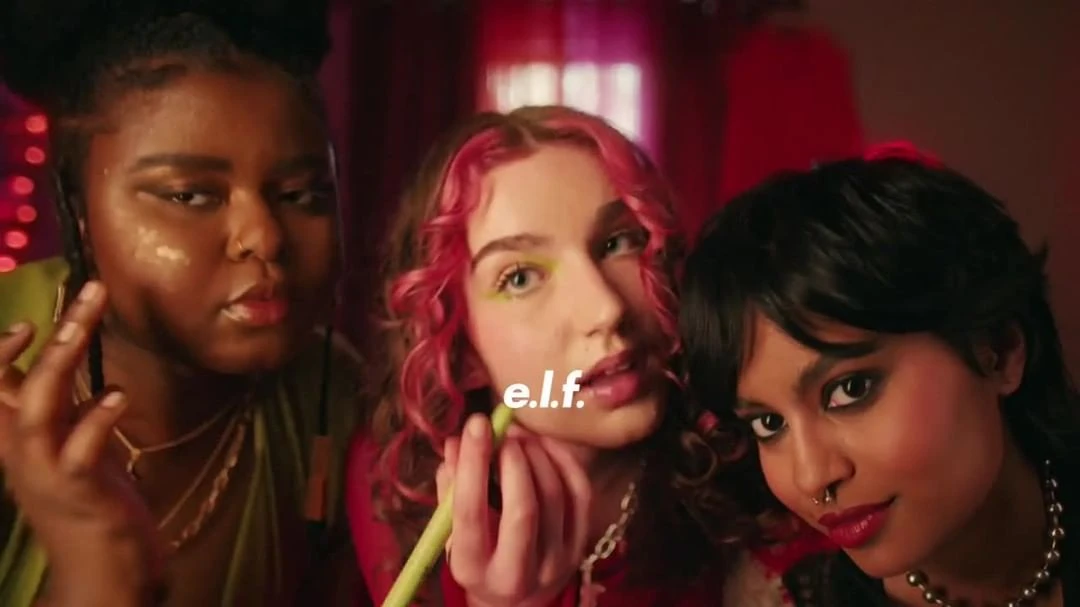Three diverse young women pose indoors with soft lighting, highlighting their makeup, hairstyles, and fashion choices in a close-up shot.