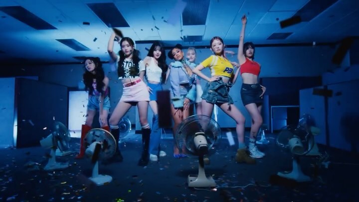 Seven young women pose indoors with vintage fans and confetti, showcasing coordinated outfits and dynamic poses in a vibrant, dynamic scene.