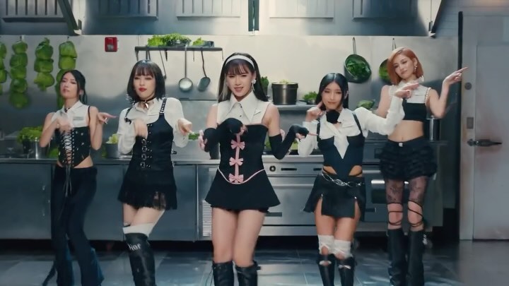 Five women in fashionable outfits dancing in a kitchen-like setting, showcasing unique styles and poses in a well-lit environment.