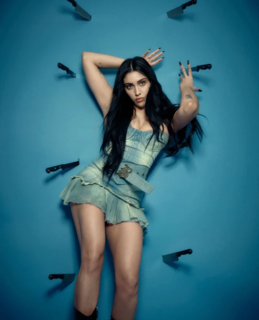 Young woman in a blue dress poses against a blue wall, surrounded by knives. Long dark hair, dark manicure, portrait orientation.