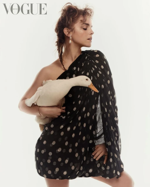 Emma Watson poses with a white duck in a fashion editorial wearing a black and white polka dot dress against a light background.