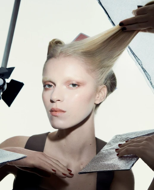 Blonde woman with stylized hair poses in a studio setting with lighting equipment and silver reflectors. Fashion and beauty shot.