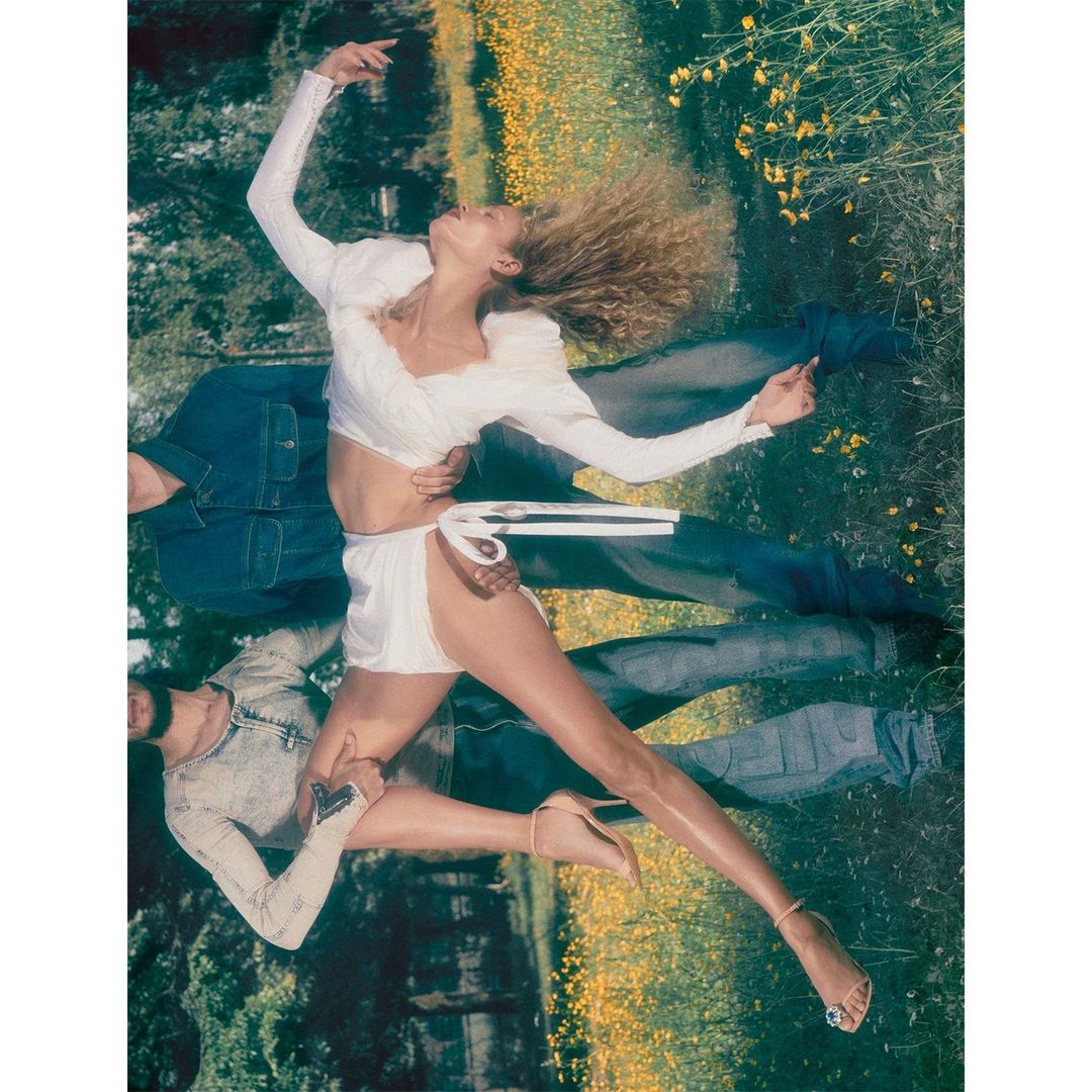 Fashion photo of a woman in white outfit with two partial figures in denim posing against a meadow backdrop.