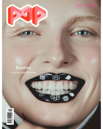 Close-up portrait of a smiling woman with black lipstick adorned with white floral motifs, photographed by Charlotte Wales.