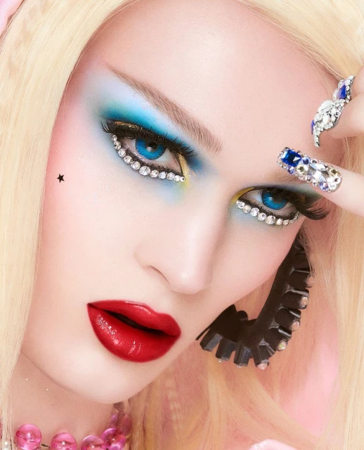 Close-up of a woman with glamourous makeup, including blue eyeshadow, bright red lips, jewel-encrusted nails, and distinctive earrings.