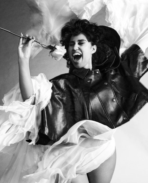 Monochrome portrait of a woman with curly hair wearing a leather jacket, holding a rose and tulle in a photo studio setting.