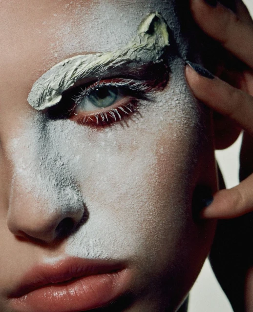 Close-up portrait of a woman with painted face, green eye shadow and dark nail polish. Beauty and fashion photography.