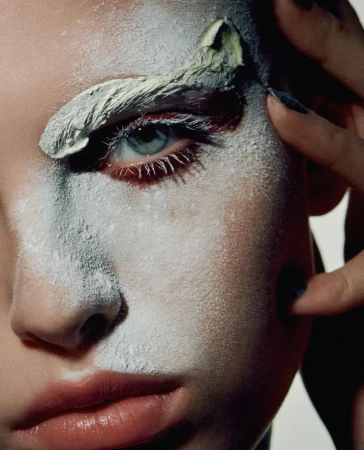 Close-up portrait of a woman with painted face, green eye shadow and dark nail polish. Beauty and fashion photography.