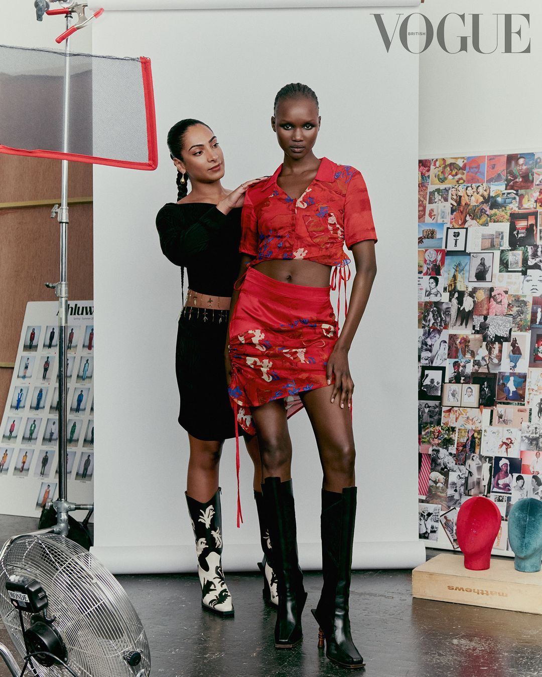 Editorial fashion shot in studio features two women; one Black model in red floral skirt and crop top and other posing in black.