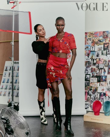 Editorial fashion shot in studio features two women; one Black model in red floral skirt and crop top and other posing in black.