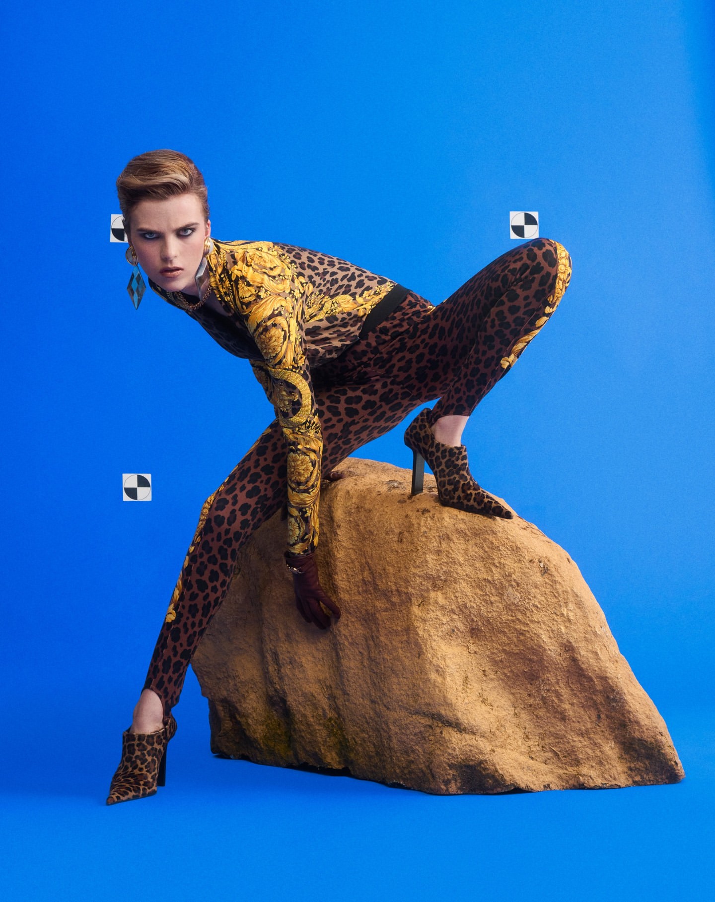 Model in leopard print bodysuit crouched on a large rock against a solid blue background by Charlotte Wales