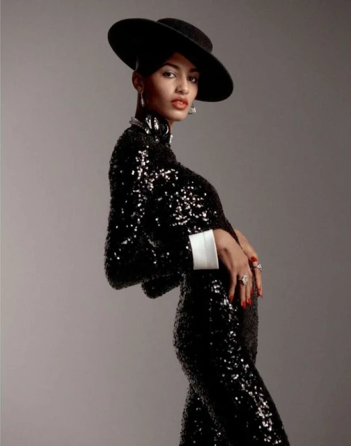 Elegant woman in a black sequin gown and hat posing in a studio setting. Fashionable attire, sophisticated style, and glamorous accessories.