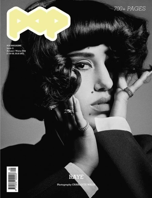 Black-and-white magazine cover portrait featuring a woman with dark curly hair and rings, wearing a dark jacket, over a gray background.
