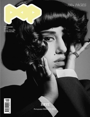 Black-and-white magazine cover portrait featuring a woman with dark curly hair and rings, wearing a dark jacket, over a gray background.