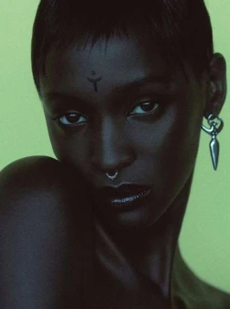 Close-up portrait of a woman with short dark hair, forehead marking, and silver earrings against a lime green background