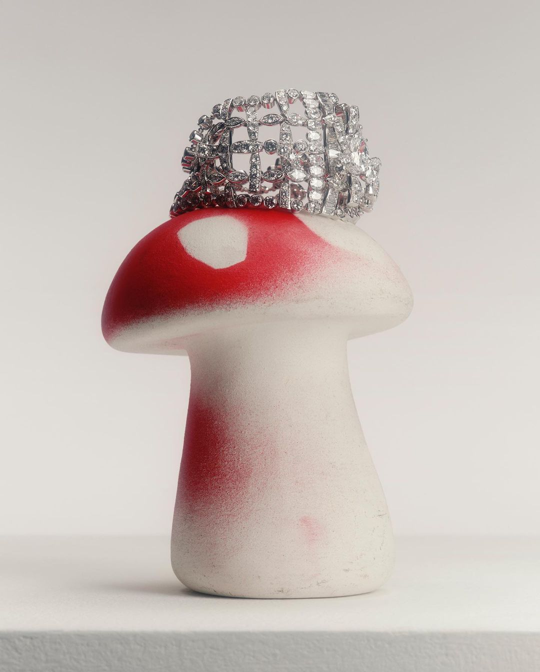 Close-up of a decorative silver bracelet sitting on top of a white and red mushroom-shaped statue in a neutral setting.