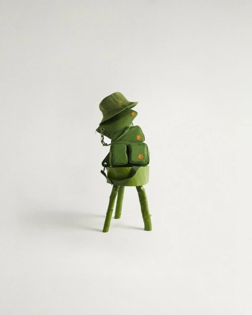 Still life shot of a green bucket hat and two small bags stacked on a green faux-wood stand against a light grey background.