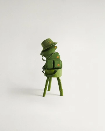 Still life shot of a green bucket hat and two small bags stacked on a green faux-wood stand against a light grey background.