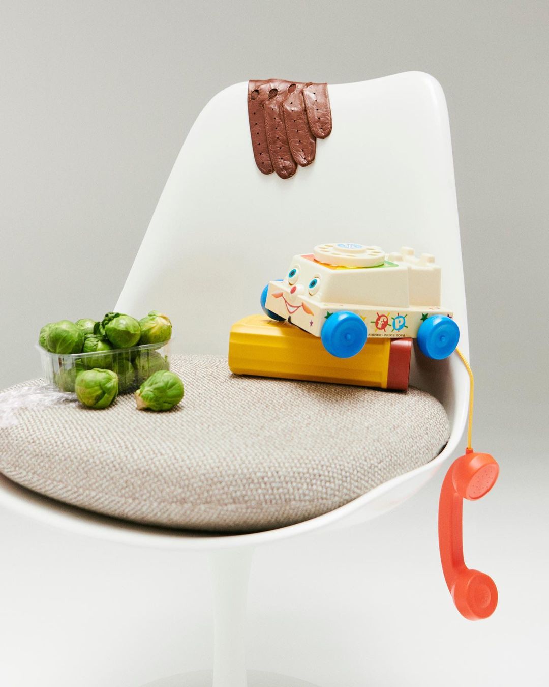 Still life of Brussels sprouts and a toy car on a white chair against a neutral background. Brussels sprouts in container.