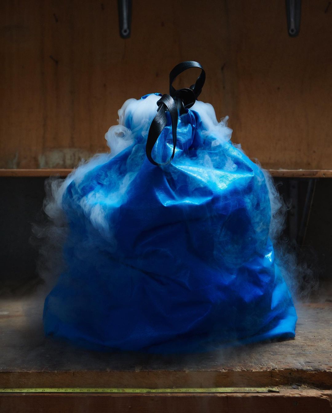 A blue plastic-like object encircled by white smoke, held by a black strap against a simple brown background, creating a mysterious visual.
