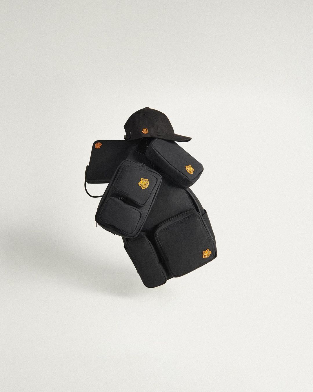 Black backpack with multiple detachable pouches and a black baseball cap featuring a yellow logo, presented against a white backdrop.