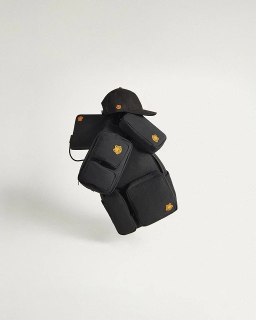Black backpack with multiple detachable pouches and a black baseball cap featuring a yellow logo, presented against a white backdrop.