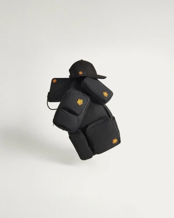 Black backpack with multiple detachable pouches and a black baseball cap featuring a yellow logo, presented against a white backdrop.