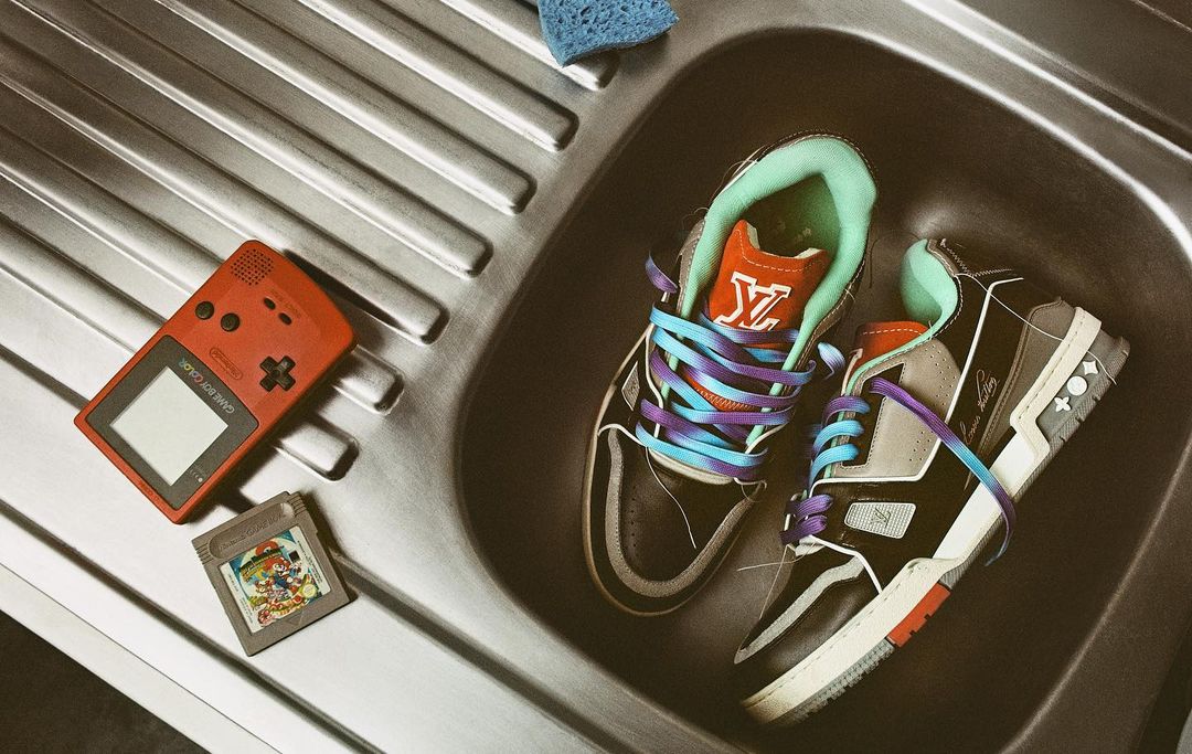 Two Louis Vuitton sneakers and a Game Boy in a silver sink with a blue sponge and a game cartridge for a stylish, retro gamer image.