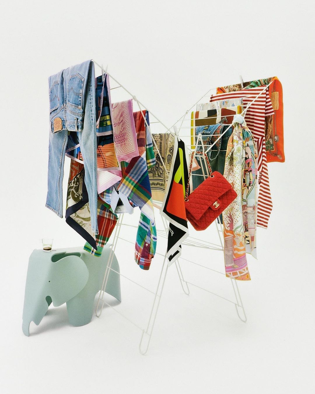 Colorful array of clothing items hanging on a white drying rack with an elephant-shaped table against a white background.