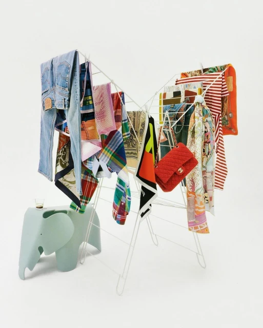 Colorful array of clothing items hanging on a white drying rack with an elephant-shaped table against a white background.