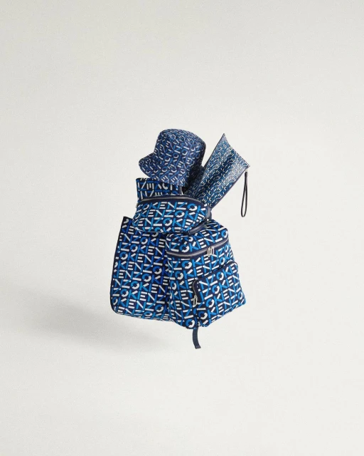 Studio shot of a blue backpack with the Kenzo logo pattern paired with a bucket hat and flat pouch, all against a clean white background.