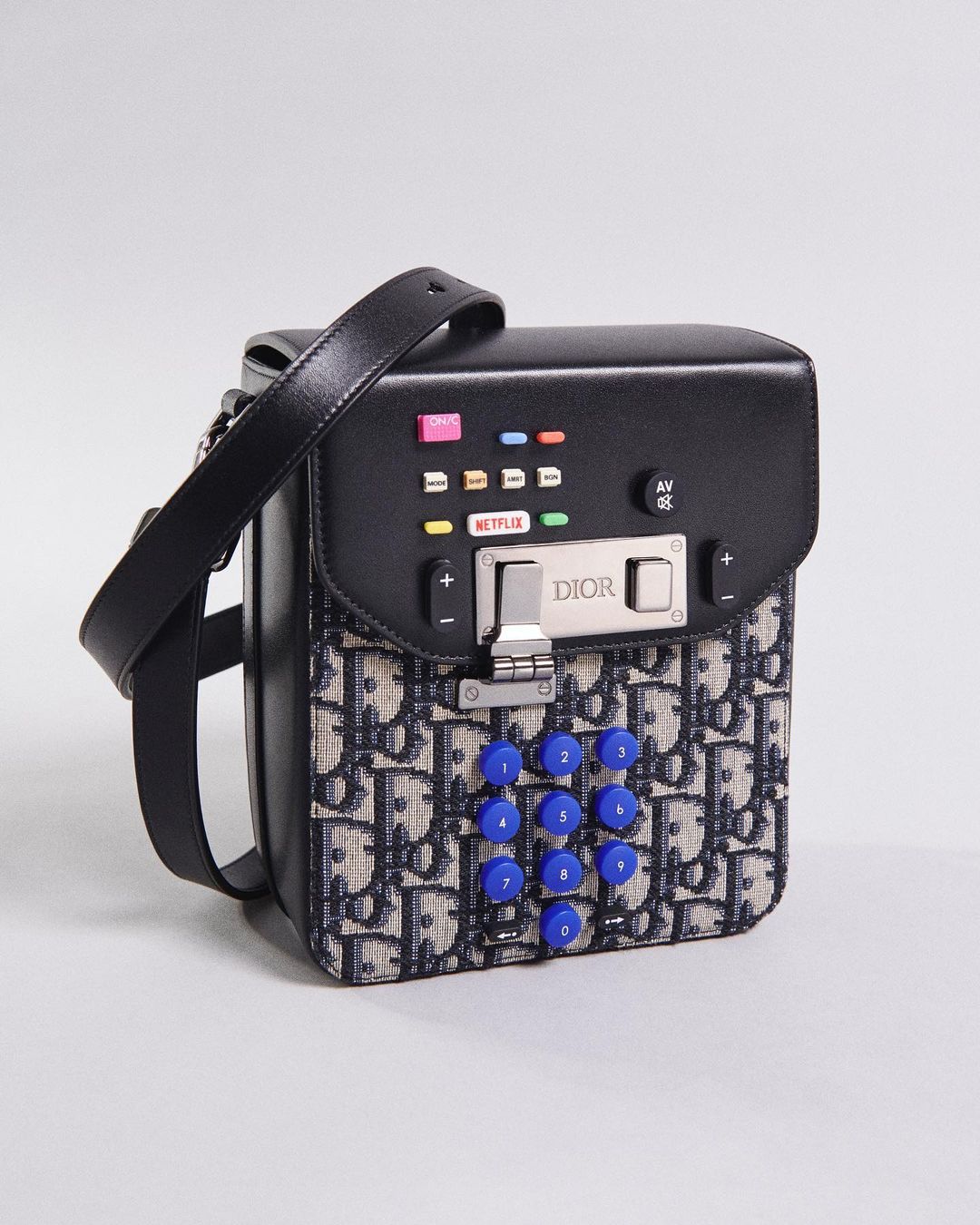 Close-up of a black Dior handbag with a phone keypad design, featuring the Dior logo, silver hardware, and colorful accents on a gray background.