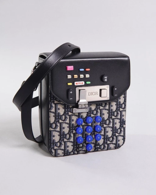Close-up of a black Dior handbag with a phone keypad design, featuring the Dior logo, silver hardware, and colorful accents on a gray background.