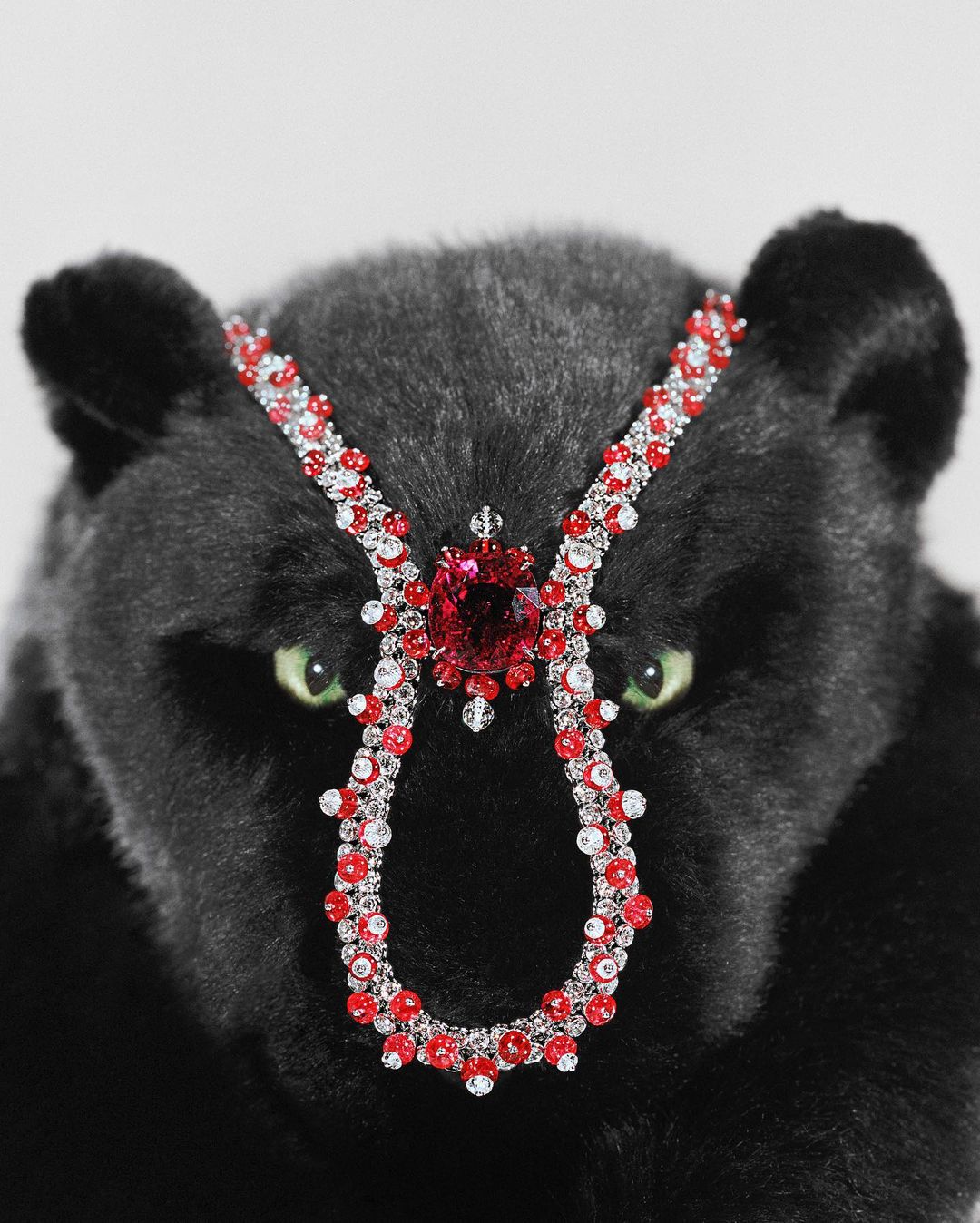 Close-up of a black panther plush toy adorned with an elaborate red and clear beaded headpiece against a plain white background.