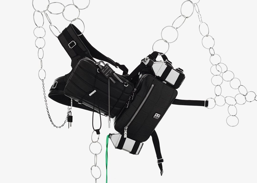 Suspended black nylon bags with silver accents are connected by black straps and chains against a bright white backdrop with silver rings.