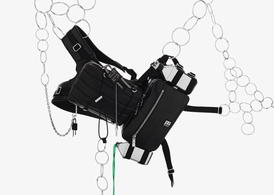 Suspended black nylon bags with silver accents are connected by black straps and chains against a bright white backdrop with silver rings.