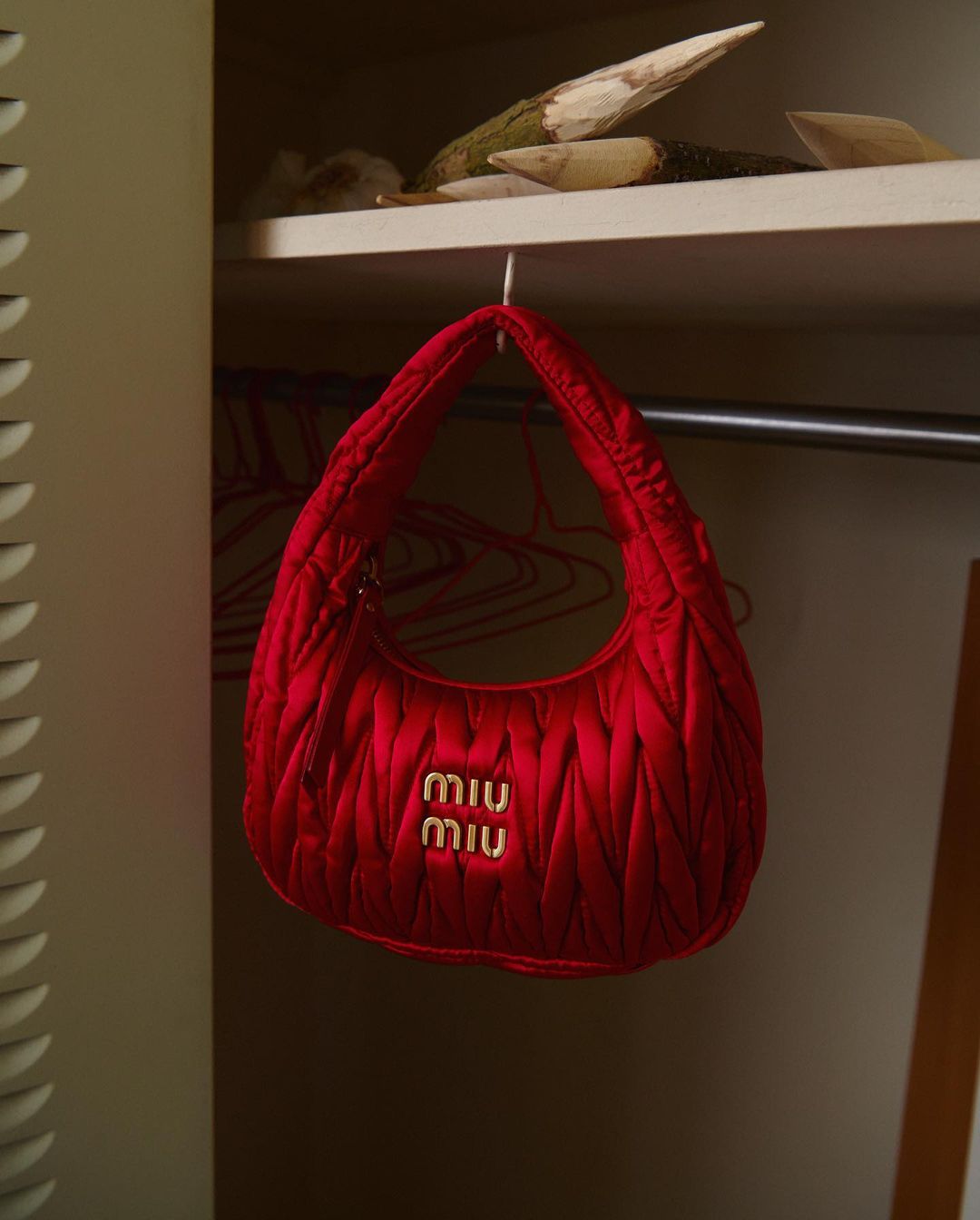 Close-up shot of a vibrant red Miu Miu quilted handbag hanging inside a closet, showcasing its texture and luxury branding.