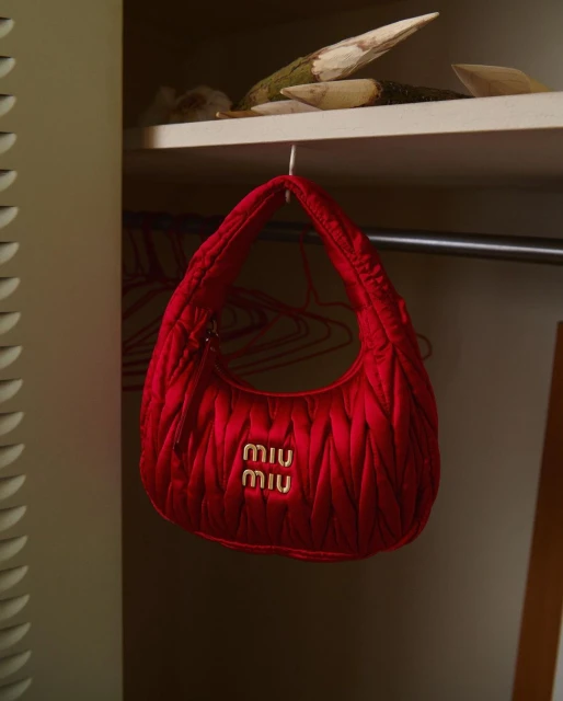 Close-up shot of a vibrant red Miu Miu quilted handbag hanging inside a closet, showcasing its texture and luxury branding.