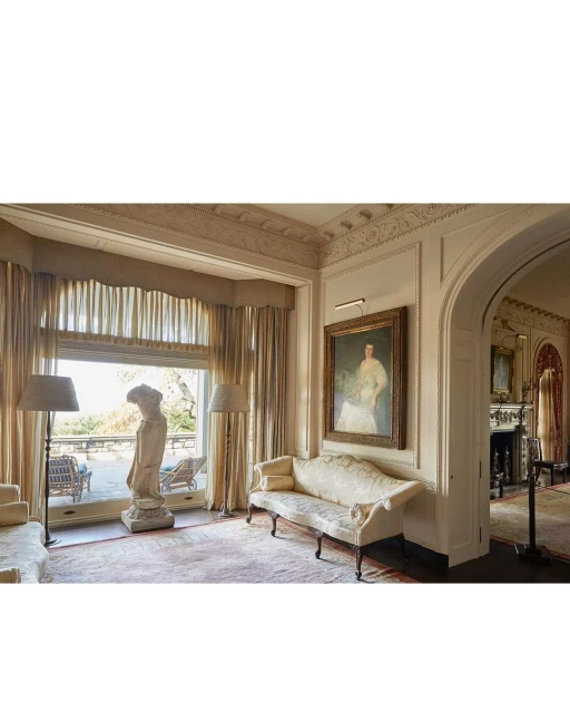 Ornate living room with a statue, painting, and lounge furniture, offering a glimpse of an outdoor patio, bathed in soft, natural light.