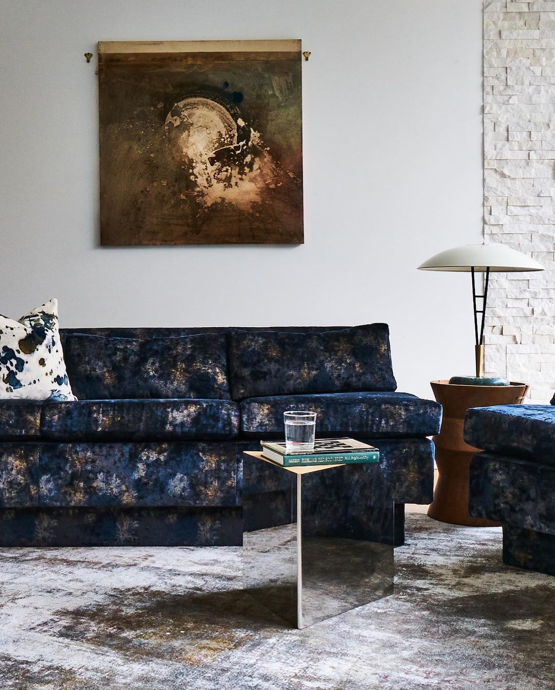Living room interior featuring a blue patterned sofa, side table with books and glass, and decorative wall art in a neutral colour palette.