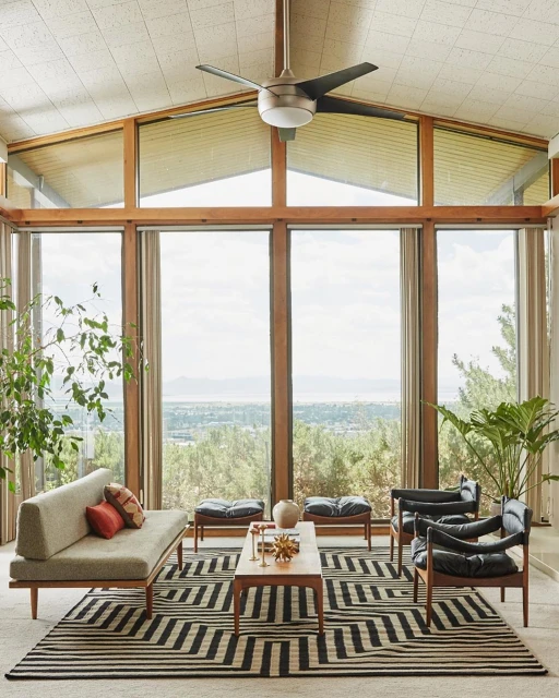 Living room featuring mid-century modern furniture, chevron pattern rug, floor-to-ceiling windows with a view, and indoor plants.