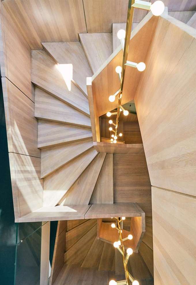 High-angle shot showcases a modern wooden spiral staircase indoors, complemented by a golden light fixture, highlighting interior design elements.